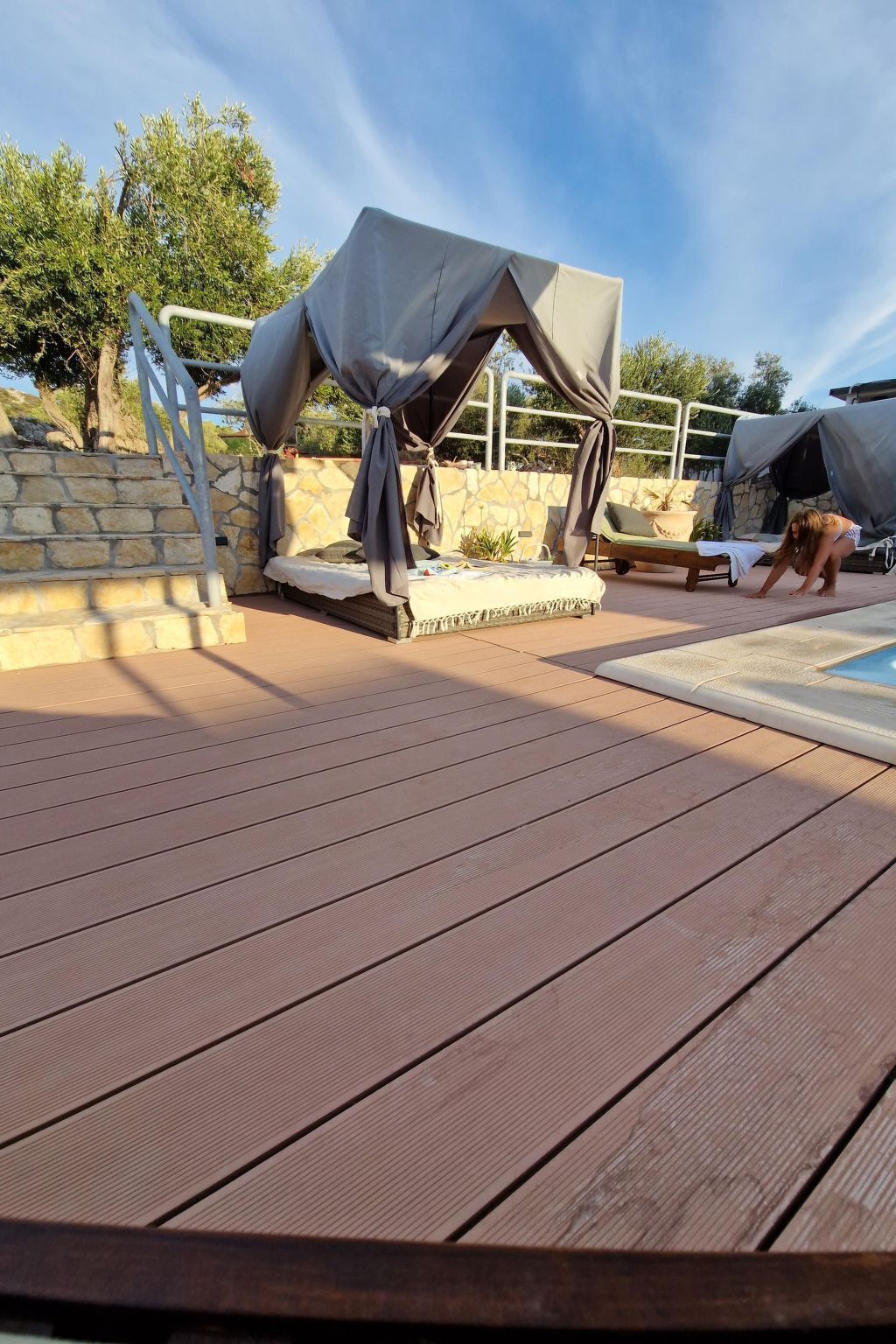 Una terraza de madera con zona de estar cubierta y una piscina.