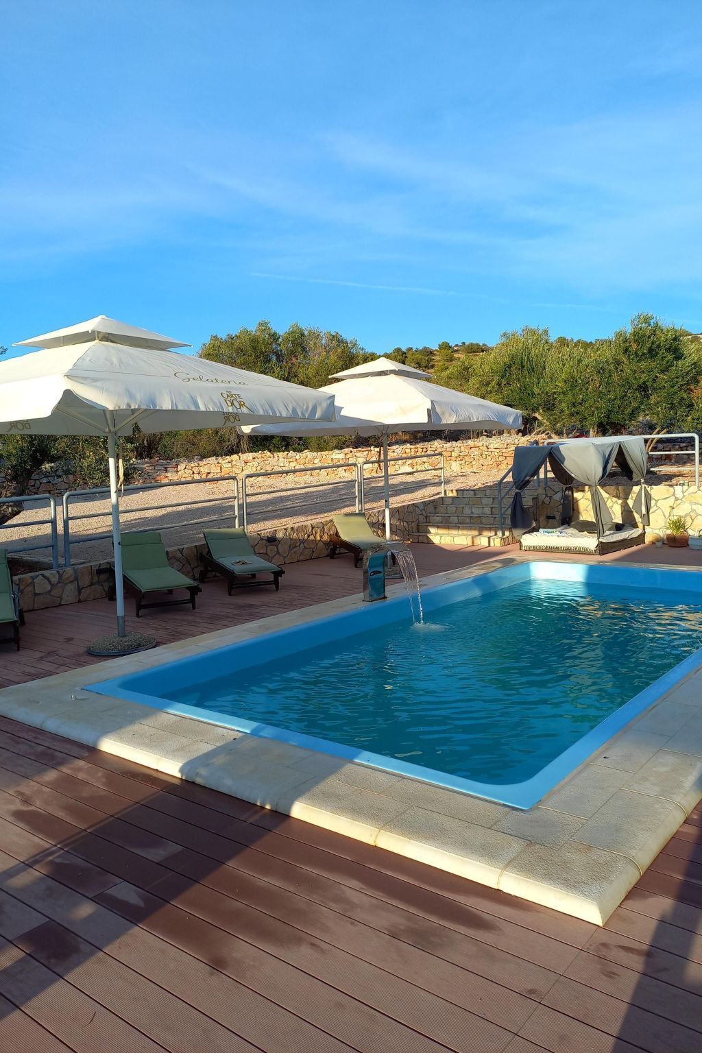 A swimming pool with lounge chairs and umbrellas, surrounded by stone walls and greenery.