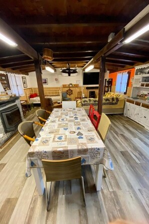 A dining area with a long table covered with a patterned tablecloth, surrounded by wooden chairs.