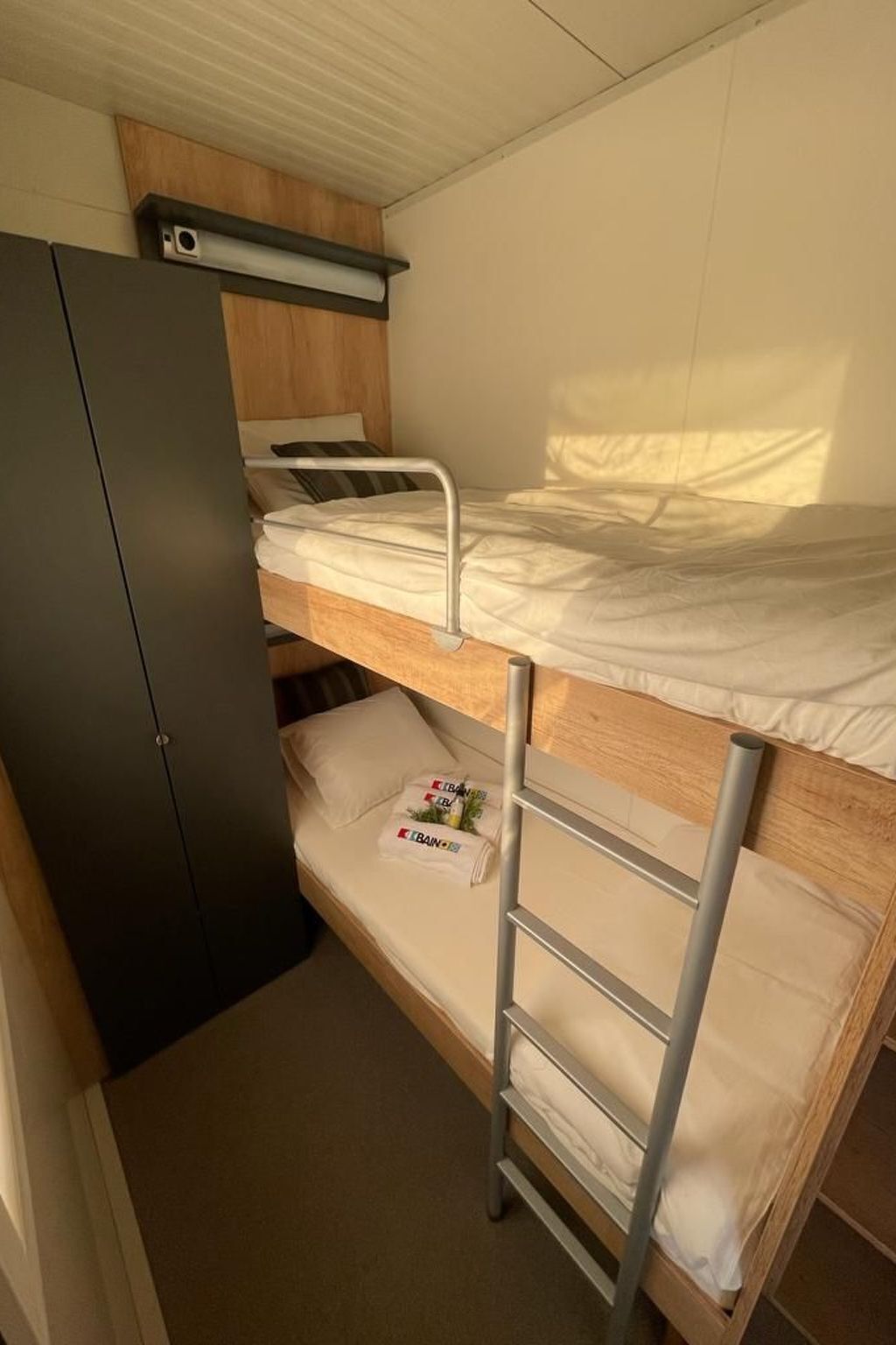 Letto a castello con scaletta, una piccola scrivania e un armadio in una stanza compatta.