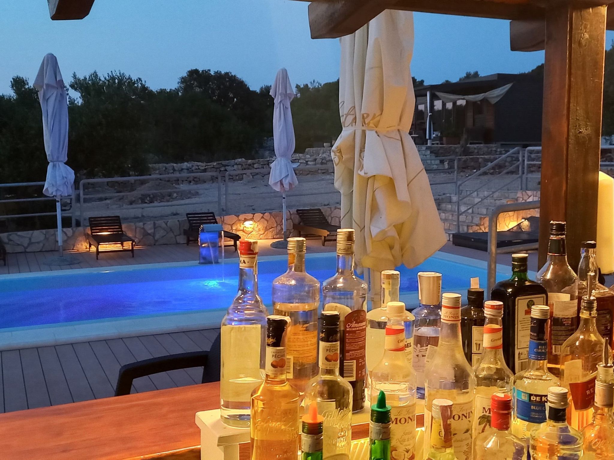 Ein Barbereich am Pool mit verschiedenen Spirituosen, einem Pool und Außenmöbeln mit Sonnenschirmen.