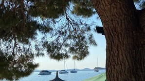 A stone-paved beach area with lounge chairs and a thatched umbrella, overlooking calm waters with boats. - Strandhaus Sofia - Ferienanlage Bain, Žut - Kornati by Interhome (Dragišina)
