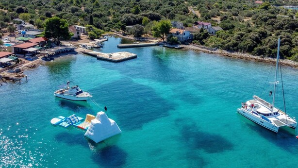 A coastal village with clear turquoise waters, boats docked at the harbor, and houses along the shore. - Strandhaus Sofia - Ferienanlage Bain, Žut - Kornati by Interhome (Dragišina)