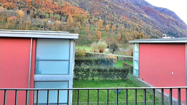 Une vue d’un paysage montagneux aux couleurs automnales, avec un champ verdoyant et un bâtiment rouge au premier plan.