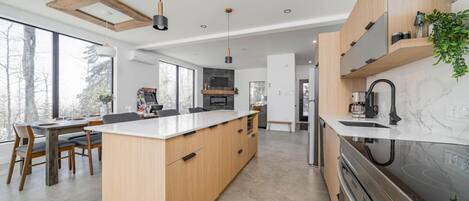 A modern kitchen with a central island, wooden cabinets, and a large window overlooking a snowy landscape.