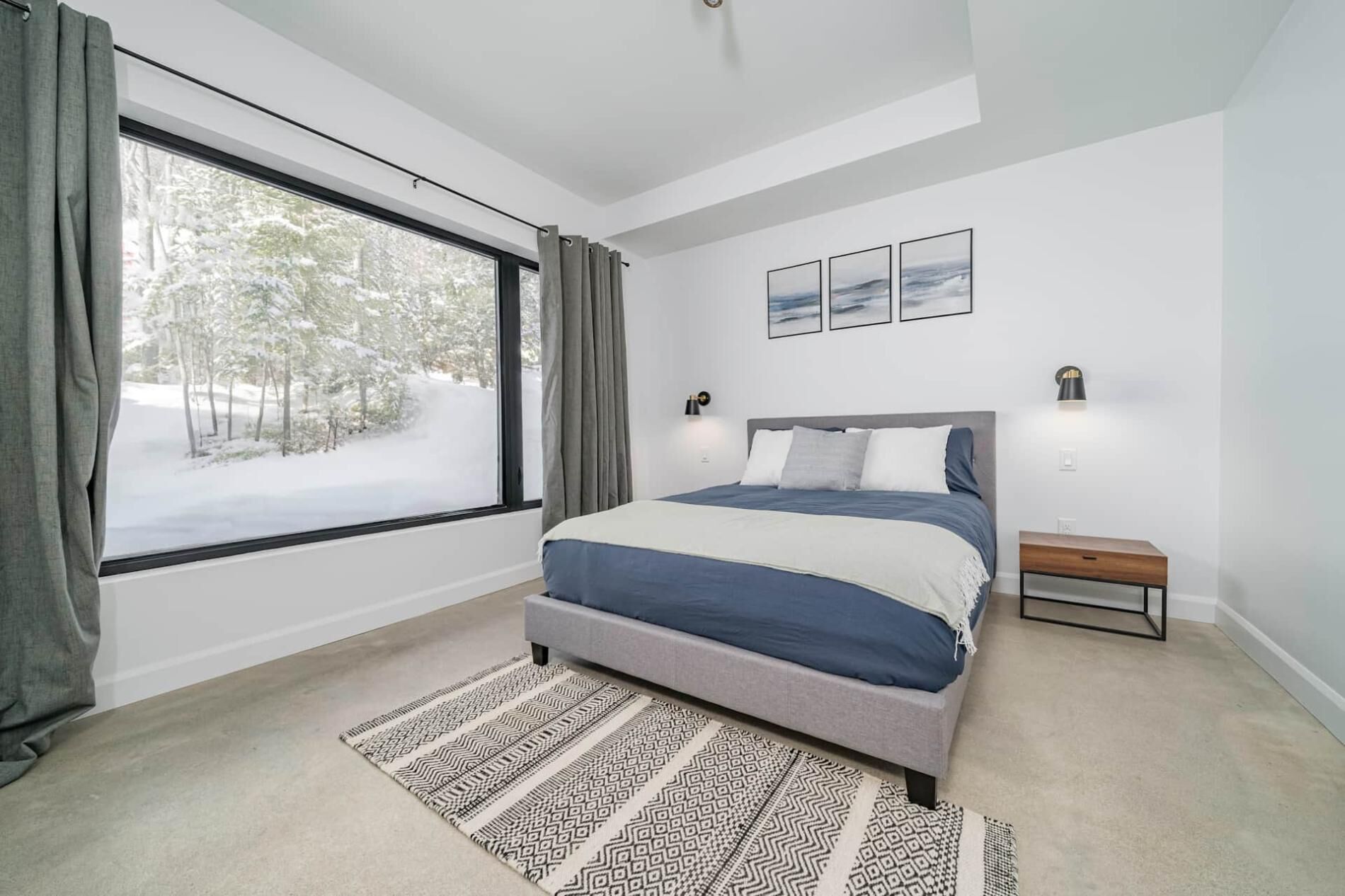 A modern bedroom with a large window, a bed with a headboard, a bedside table, and a rug.