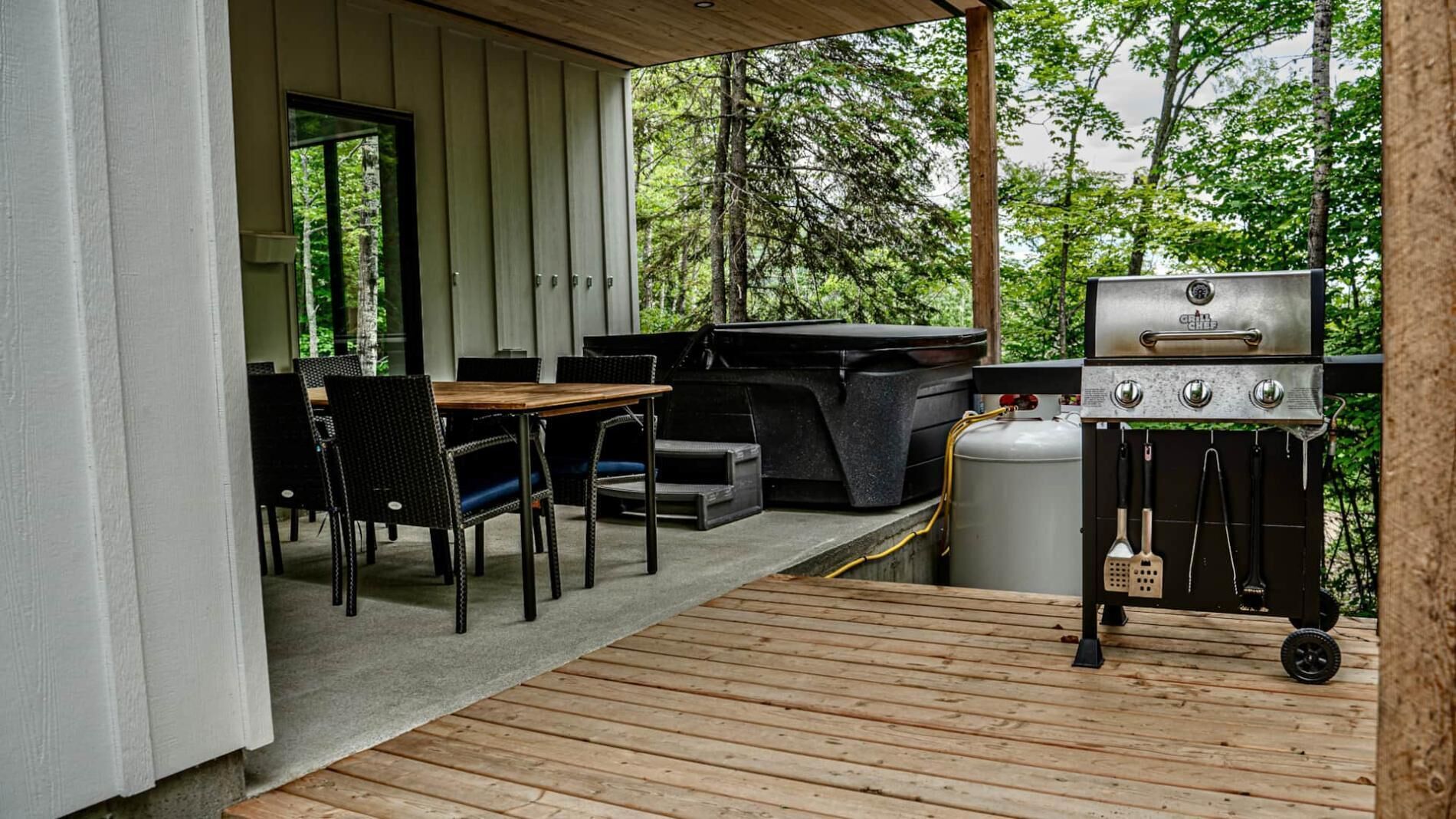 An outdoor patio with a grill, seating area, and a view of the forest.