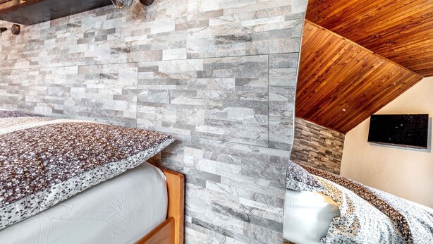 Un dormitorio con pared de piedra simulada, techo de madera y cama con colcha estampada de flores.