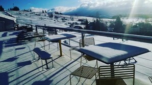 Zona de estar exterior cubierta de nieve, con mesas y bancos, con vistas a un paisaje nevado y una pista de esquí.