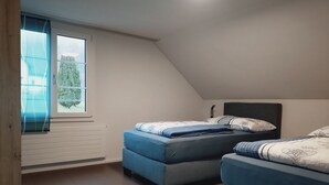 Une chambre avec deux lits, une fenêtre avec des rideaux, un radiateur et une vue sur la verdure à l’extérieur.