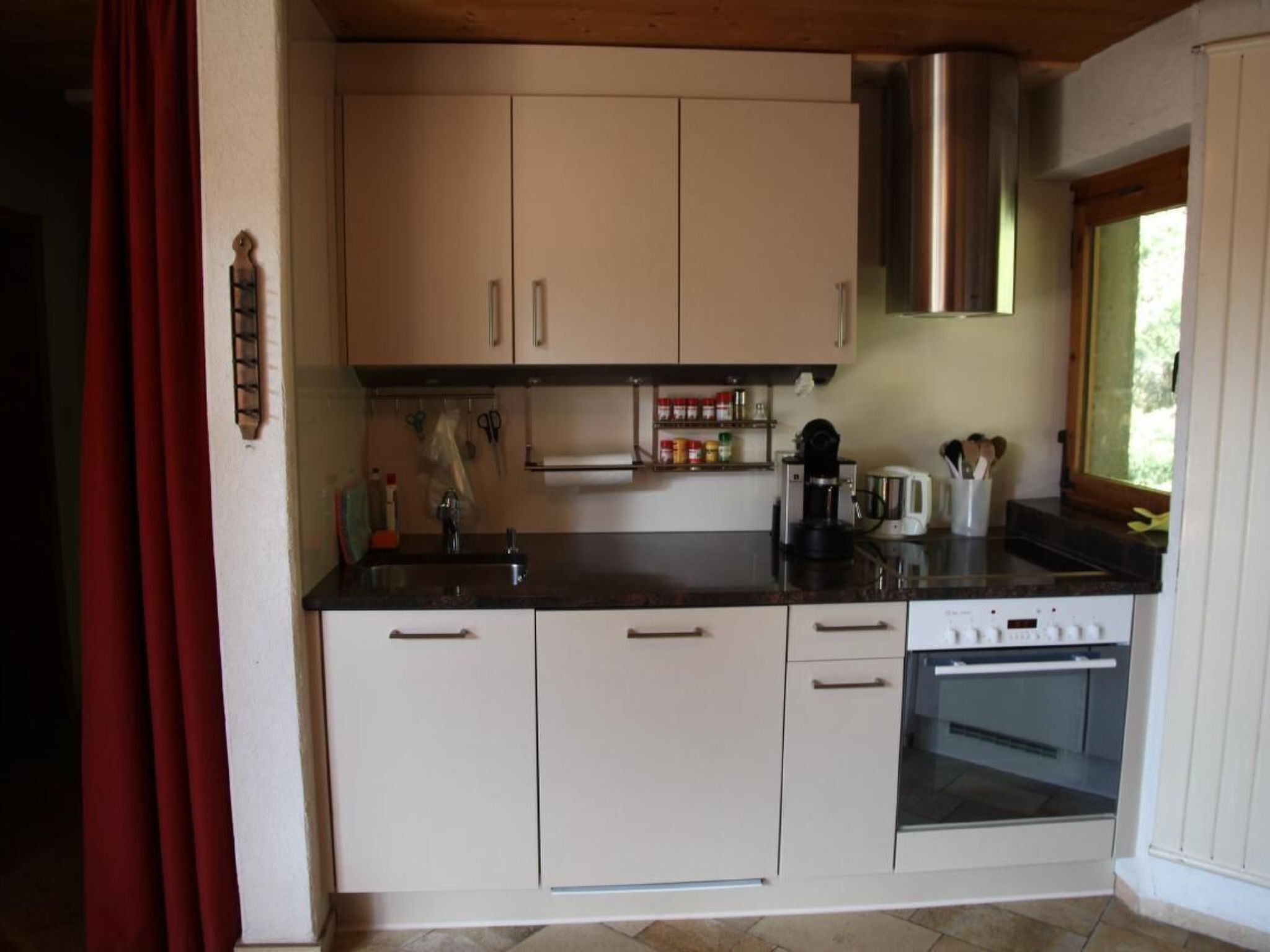 Eine kleine Küche mit weißen Schränken, einer Edelstahl-Dunstabzugshaube, einer Kaffeemaschine und einem Toaster.