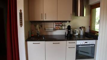 Eine kleine Küche mit weißen Schränken, einer Edelstahl-Dunstabzugshaube, einer Kaffeemaschine und einem Toaster.