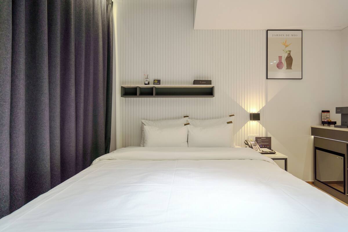 Habitación de hotel con cama, mesita de noche con teléfono, repisa en la pared y un cuadro enmarcado.