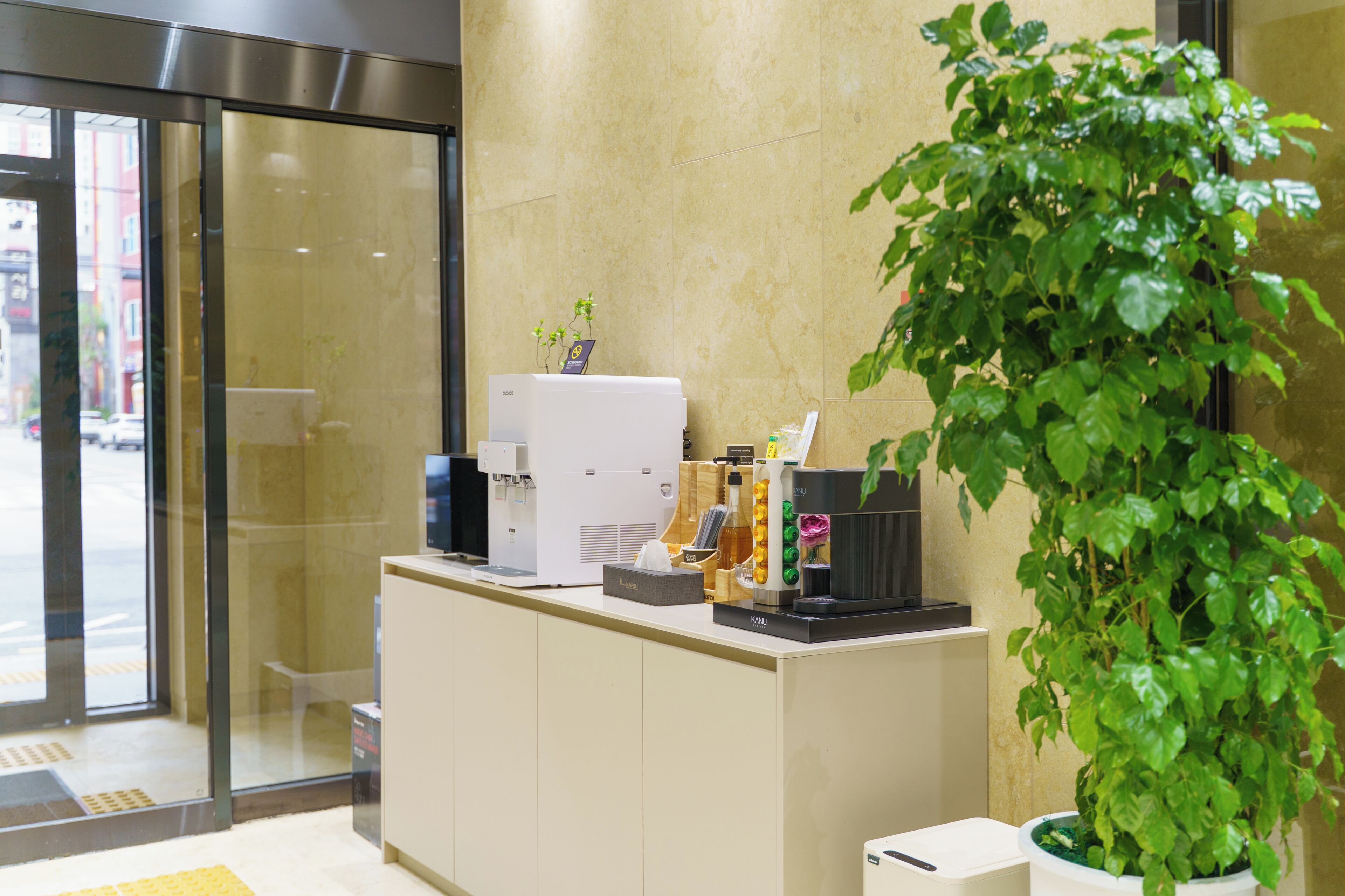 A reception desk with a coffee machine, a plant, and a trash bin.