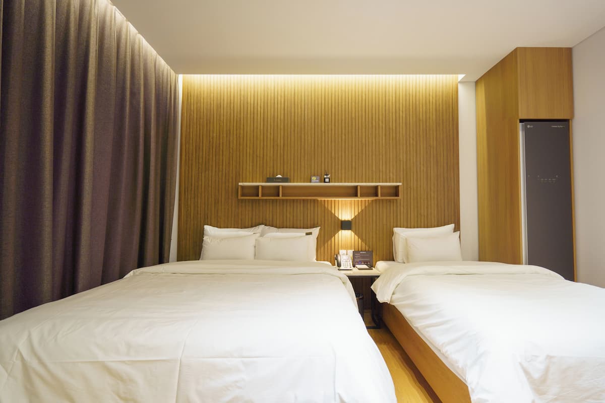 Una habitación de hotel con dos camas, una mesita de noche con lámpara y un armario empotrado.