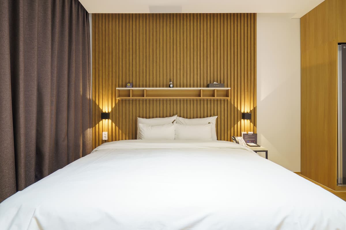 Habitación de hotel con una cama grande, cabecera de madera, mesitas de noche y una mesita auxiliar con teléfono.