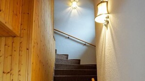 A wooden staircase with a handrail, carpeted steps, and wall-mounted lighting fixtures. - Casa Bambi 6.5 Zimmer by Interhome (Pfäfers)