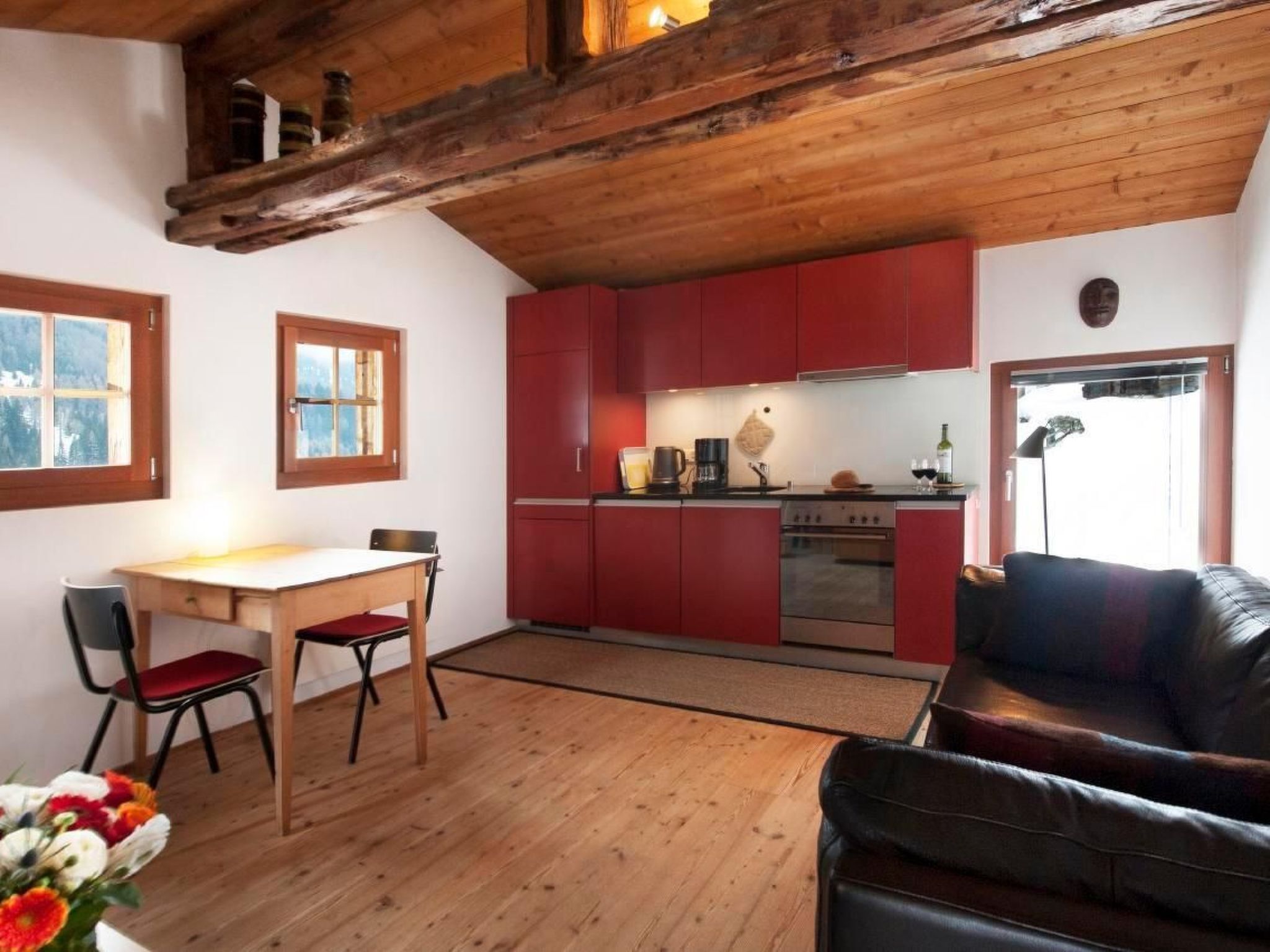 Eine gemütliche Küche mit roten Schränken, einem Holzespeisetisch und einem Ledersofa.