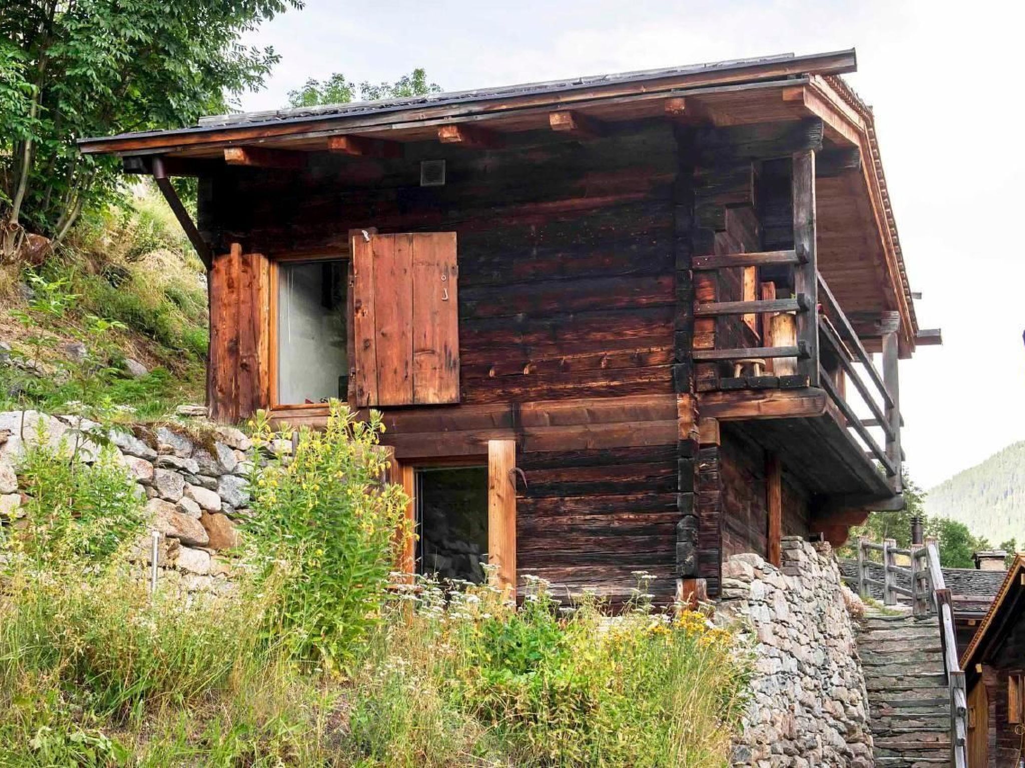 Een rustieke houten chalet met een stenen fundering, een houten trap en een balkon.