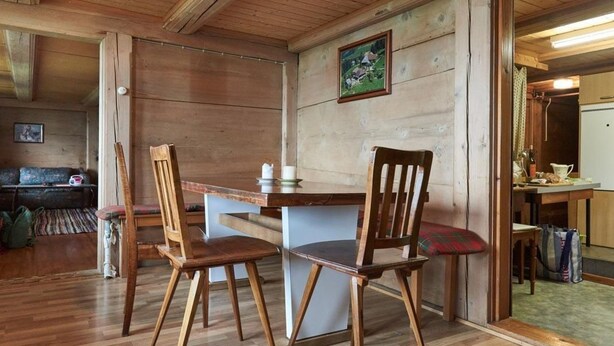 En matplats med träinredning, bestående av två stolar och ett bord, en träbänk i bakgrunden och en tavla på väggen.
