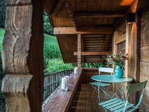 A wooden balcony with a table and chairs, a candle, and a vase with flowers.