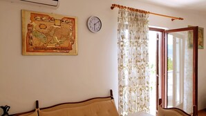 Una stanza con un letto, un tavolo coperto da una tovaglia, una sveglia, una mappa e una finestra con tende.