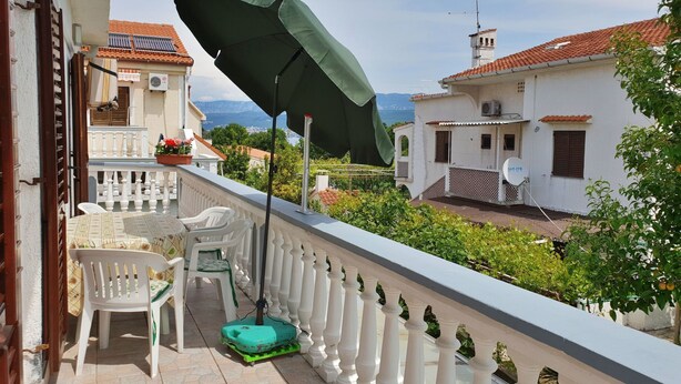 Un balcone con un ombrellone verde, sedie bianche e un tappetino verde.
