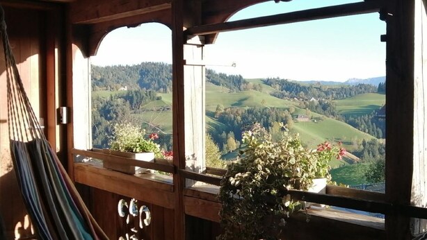 Ein Holzbalkon mit einer Hängematte und Pflanzgefäßen, mit Blick auf ein malerisches Tal.