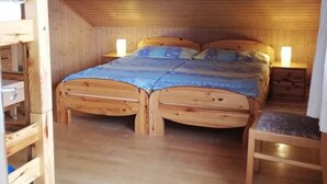 Ein Zimmer mit Holzboden, Etagenbett und Einzelbett, sowie einer geneigten Decke.