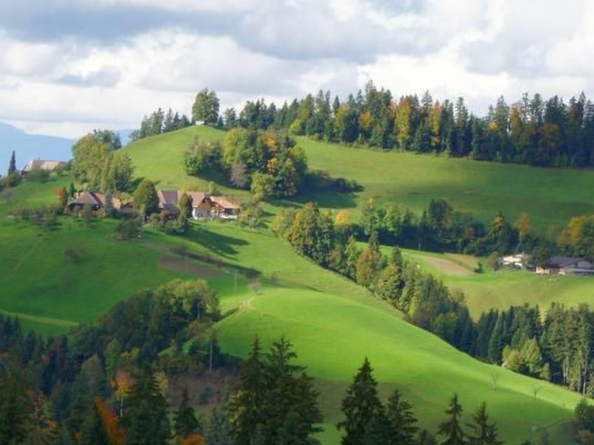 A rural landscape with rolling hills, scattered houses, and dense forests.