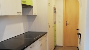 Eine schmale Küche mit weißen Schränken, einer schwarzen Arbeitsplatte und einer Holztür am Ende.