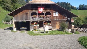 Eine Holzhütte mit Schweizer Flagge, Balkone mit Blumenkästen und einer Schotterzufahrt.