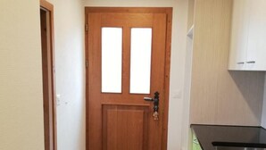 Ein schmaler Flur mit einer Holztür, einem grünen Geschirrspüler und einer schwarzen Arbeitsplatte.
