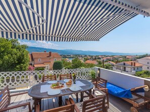 Una terraza con una mesa redonda dispuesta para comer, con vistas a una zona residencial con casas y montañas al fondo.