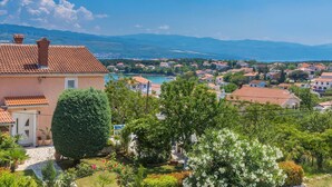 Un quartier résidentiel caractérisé par des toits recouverts de tuiles en terre cuite, une végétation luxuriante et une vue sur un lac et des montagnes lointaines.