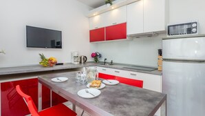 Une cuisine moderne avec des meubles blancs et rouges, un four encastré et un coin repas avec des chaises rouges et une table grise.
