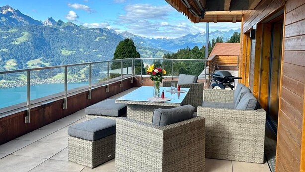 Un balcón con mobiliario de mimbre, una mesa y vistas a las montañas.