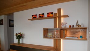 Una sala de estar moderna con una consola de madera, una estantería empotrada con objetos decorativos y un jarrón de flores en el suelo.