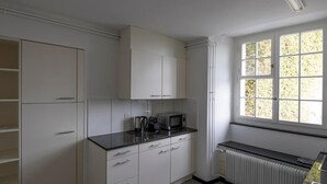 Une cuisine avec des meubles blancs, un plan de travail noir, un four à micro-ondes et une fenêtre donnant sur des arbres.