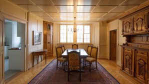 Une salle à manger avec une table et des chaises en bois, un tapis à motifs et un lustre.