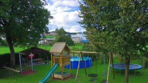Une aire de jeux avec des balançoires, un toboggan et un trampoline.
