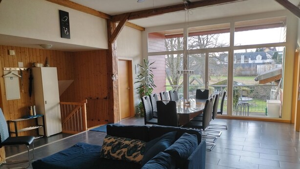 Un vaste espace de vie comprenant un canapé, une table à manger et des chaises. Une porte-fenêtre coulissante donne accès à un balcon offrant une vue sur l’extérieur.