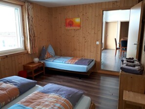 A room with wooden walls, a bed with a blue and orange bedspread, a small table with a lamp, and a painting on the wall. - Sidlers Neuhof by Interhome (Sins)