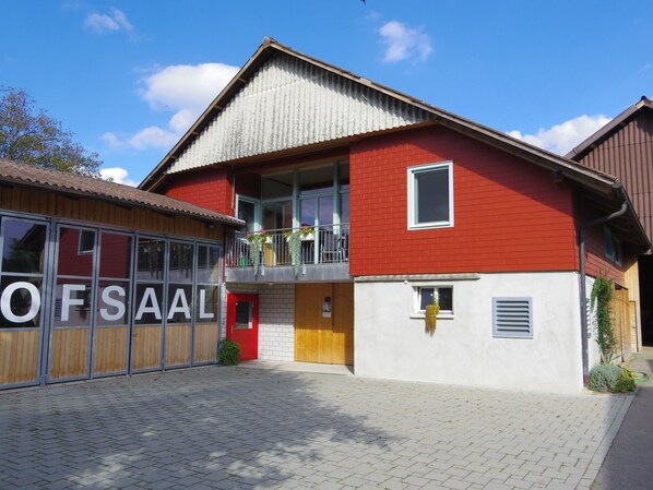 A two-story building with a red and white facade, a wooden garage door, and a balcony with hanging plants. - Sidlers Neuhof by Interhome (Sins)