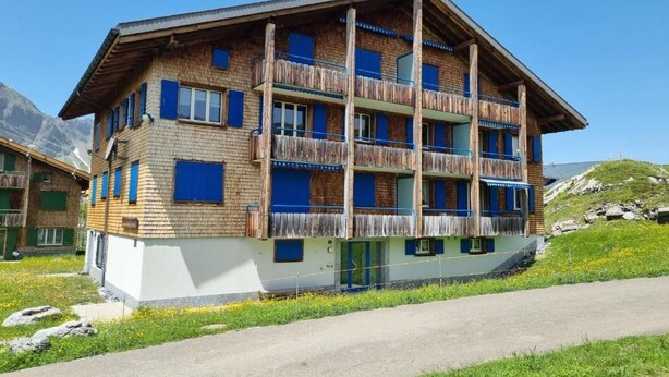 Un chalet à plusieurs étages, doté d’une façade en bois, de balcons et offrant une vue dégagée sur les montagnes environnantes.