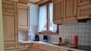 Une cuisine avec des meubles de rangement en bois, une cuisinière, une bouilloire et une fenêtre avec des rideaux.
