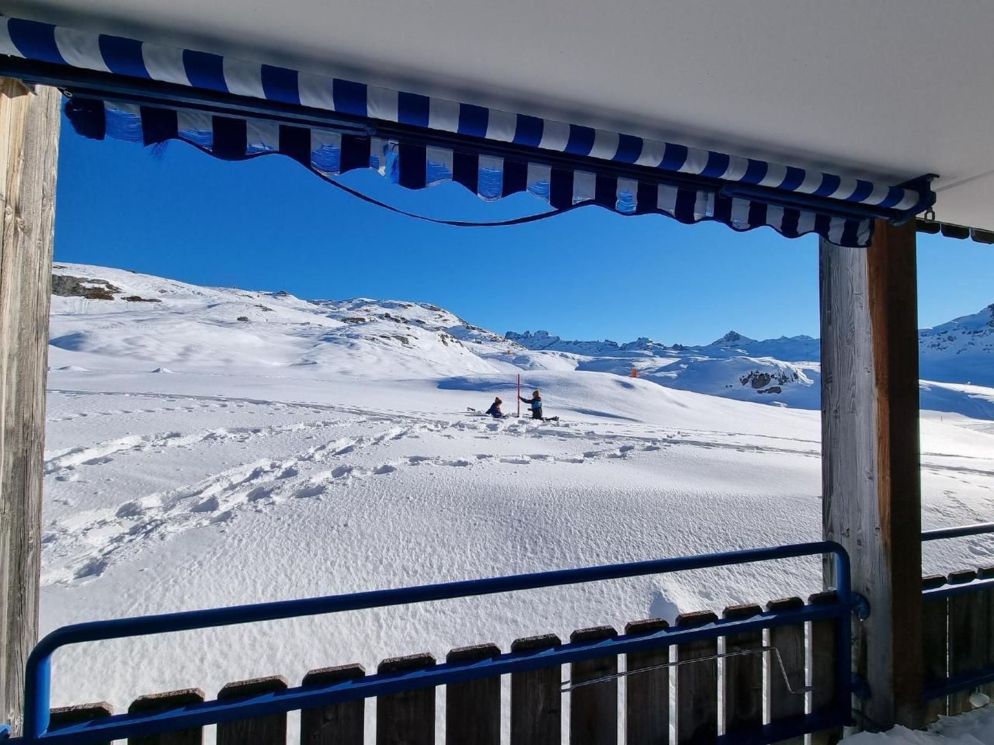 Een besneeuwd berglandschap met een houten omheining en een blauwe leuning op de voorgrond.