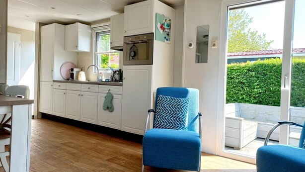 Una cocina moderna con armarios blancos, una silla azul y un amplio ventanal con vistas a la vegetación.