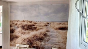 Una habitación con un mural de playa, un pequeño banco de madera y una ventana con cortina blanca.