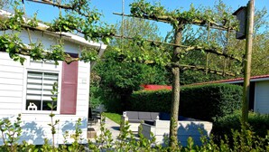 Una propiedad residencial con fachada blanca, techo rojo y un jardín con pérgola.
